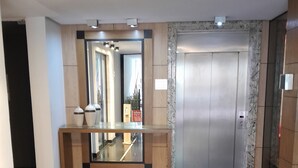 A modern lobby with a reflective floor, a reception desk, a mirror, and an elevator. - Hotel Calandre (São Paulo)