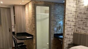 A compact hotel room with a bed, a desk, and a shower area. - Hotel Calandre (São Paulo)