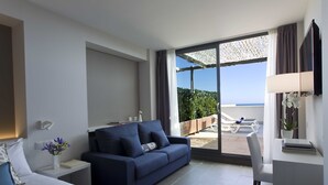 Un hotel modern amb llit, sofà, escriptori i una finestra gran que ofereix vistes al mar.