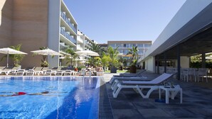 A swimming pool with lounge chairs and umbrellas, surrounded by a modern building with balconies.