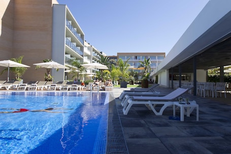 Una piscina al aire libre, sombrillas, sillones reclinables de piscina