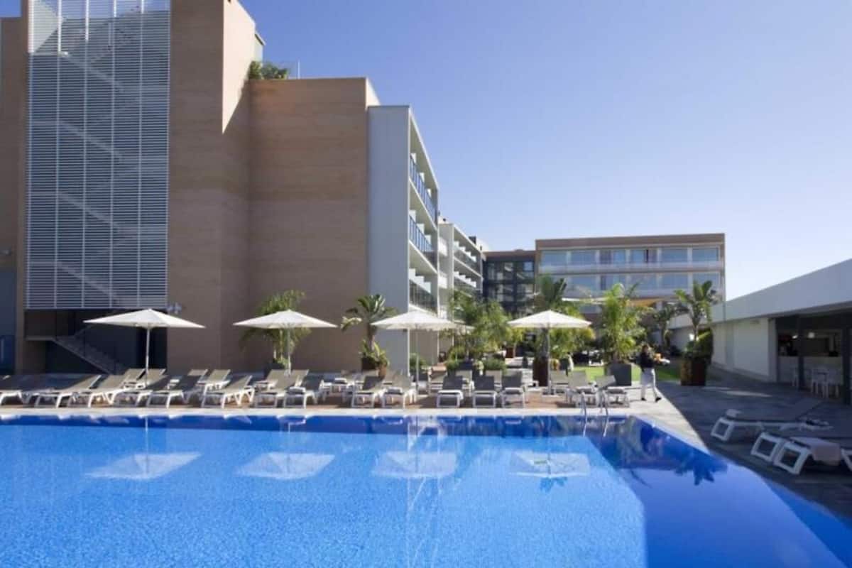 Uma piscina com espreguiçadeiras e guarda-sóis, cercada por edifícios.