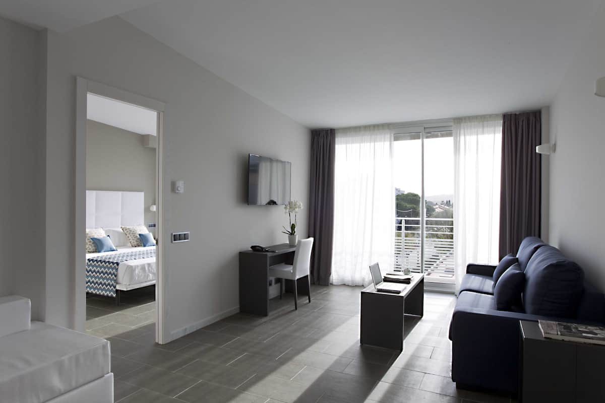 Quarto de hotel moderno com cama, escrivaninha, sofá e varanda com vista.