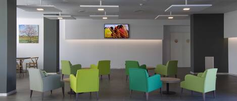 A modern lobby with green and teal chairs, a flat-screen TV, and a painting on the wall.