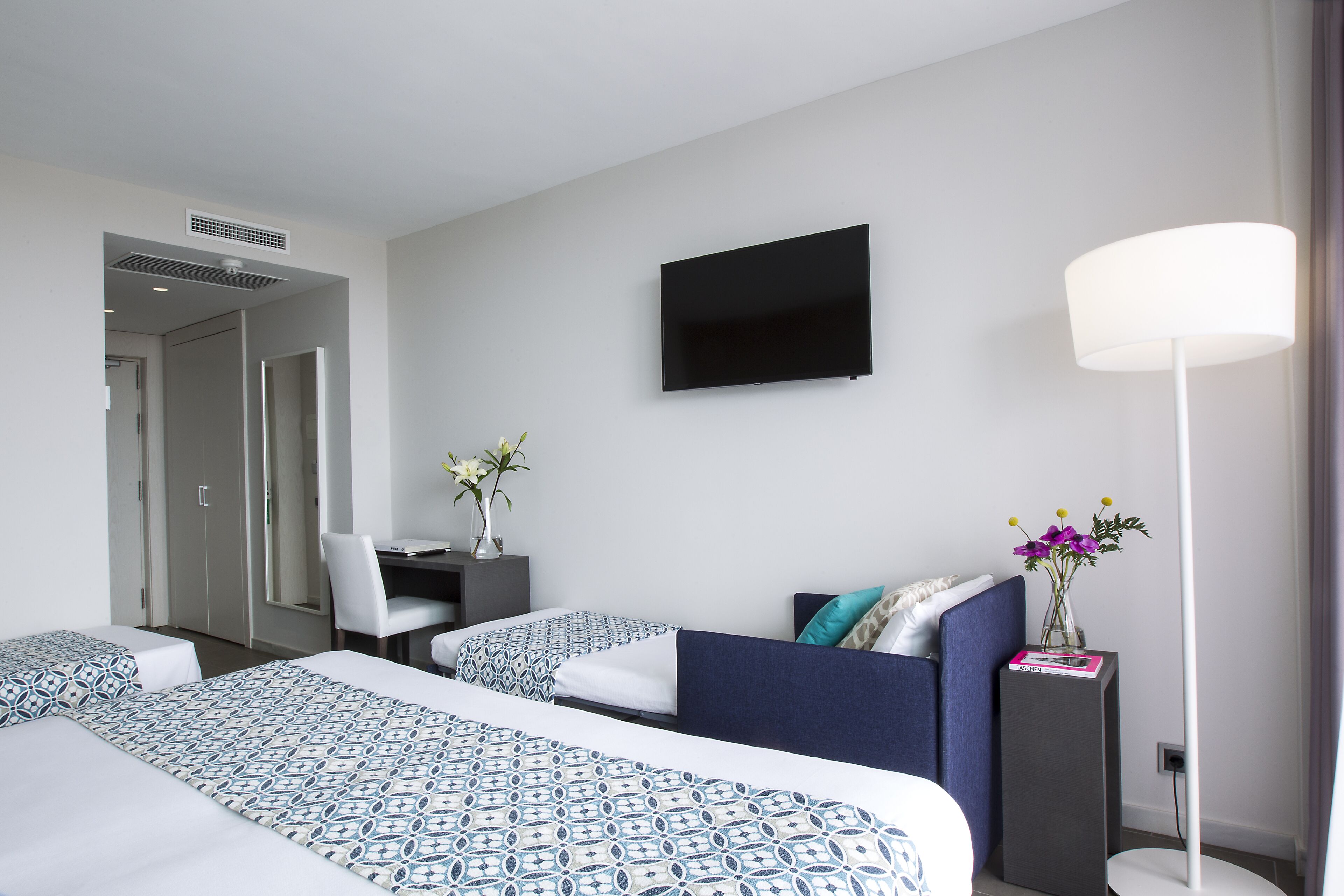Habitación de hotel con dos camas, un escritorio, una silla, un televisor y una lámpara de pie.