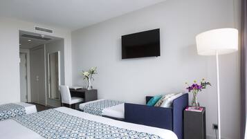 Habitación de hotel con dos camas, un escritorio, una silla, un televisor y una lámpara de pie.