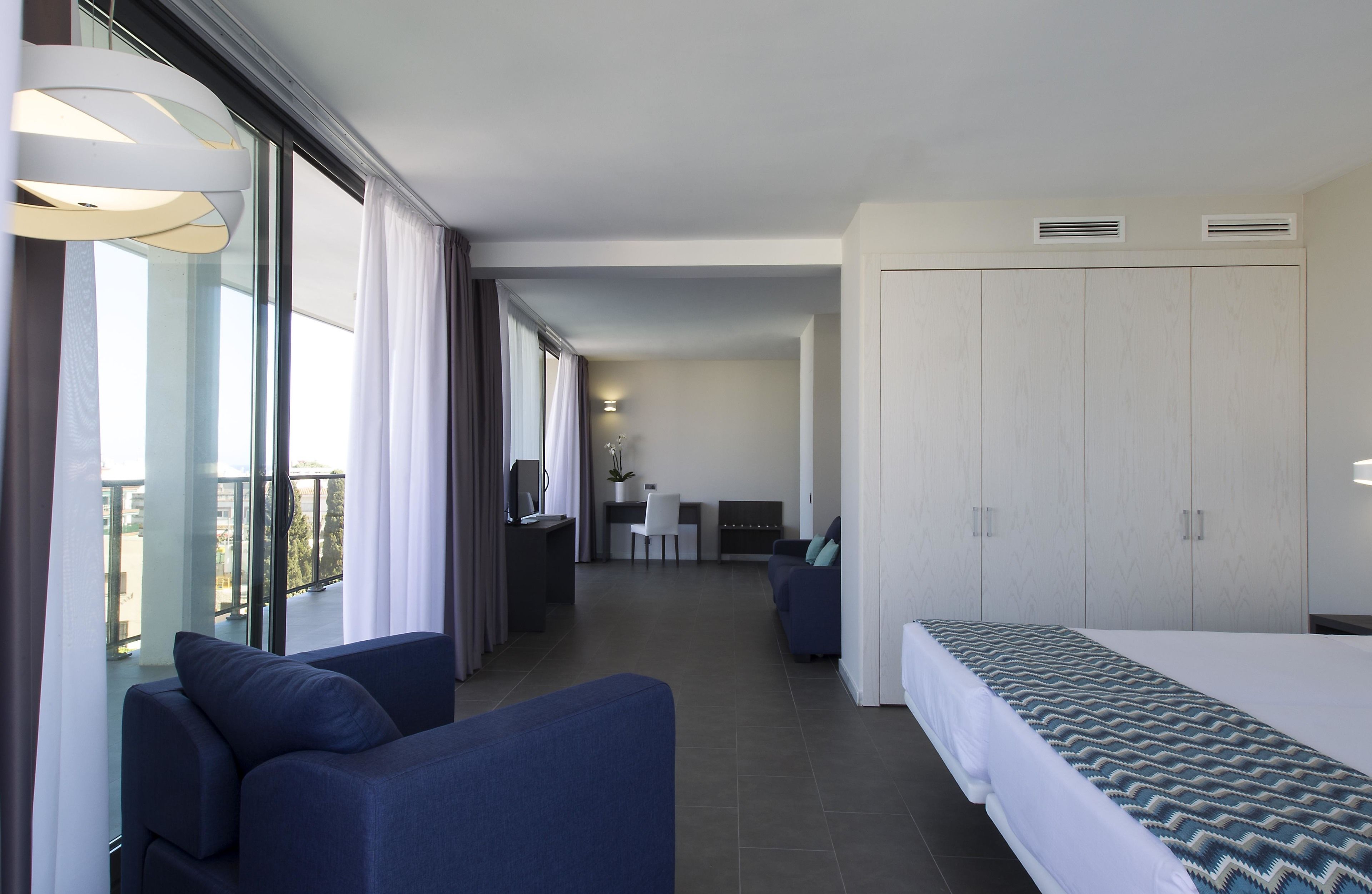 Ein modernes Hotelzimmer mit einem großen Bett, einer Couch, einem Schreibtisch und einem Balkon mit Vorhängen.