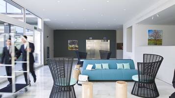 Un vestíbulo moderno con un sofá azul, sillas de mimbre negro y taburetes de madera.