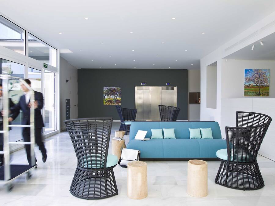 Un vestíbulo moderno con un sofá azul, sillas de mimbre negro y taburetes de madera.