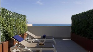 A rooftop terrace with a lounge chair, a table, and a view of the sea.