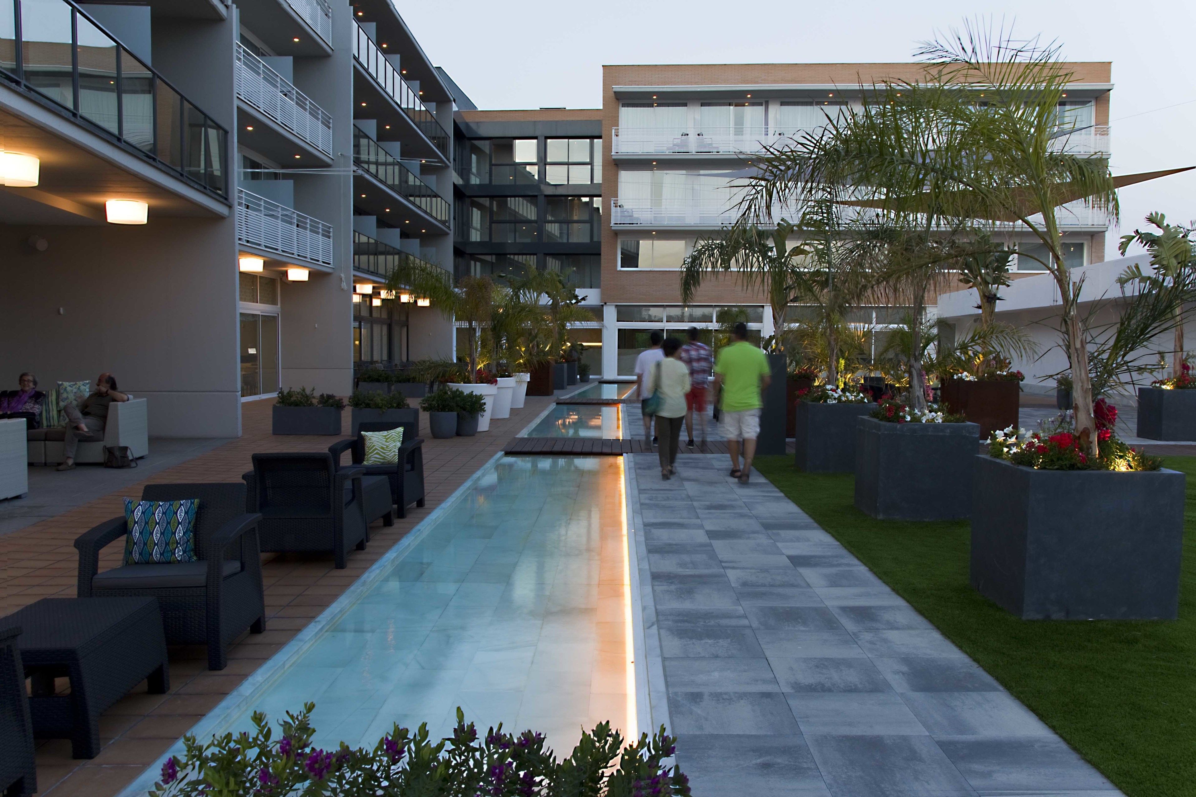 A modern outdoor pool area with lounge seating, a pathway, and a building with balconies.