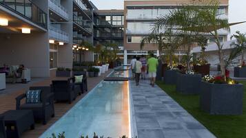 A modern outdoor pool area with lounge seating, a pathway, and a building with balconies.