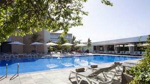 Una piscina amb gandules i ombrel·les, envoltada d'edificis i vegetació.