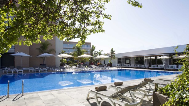 A swimming pool with lounge chairs and umbrellas, surrounded by buildings and greenery.