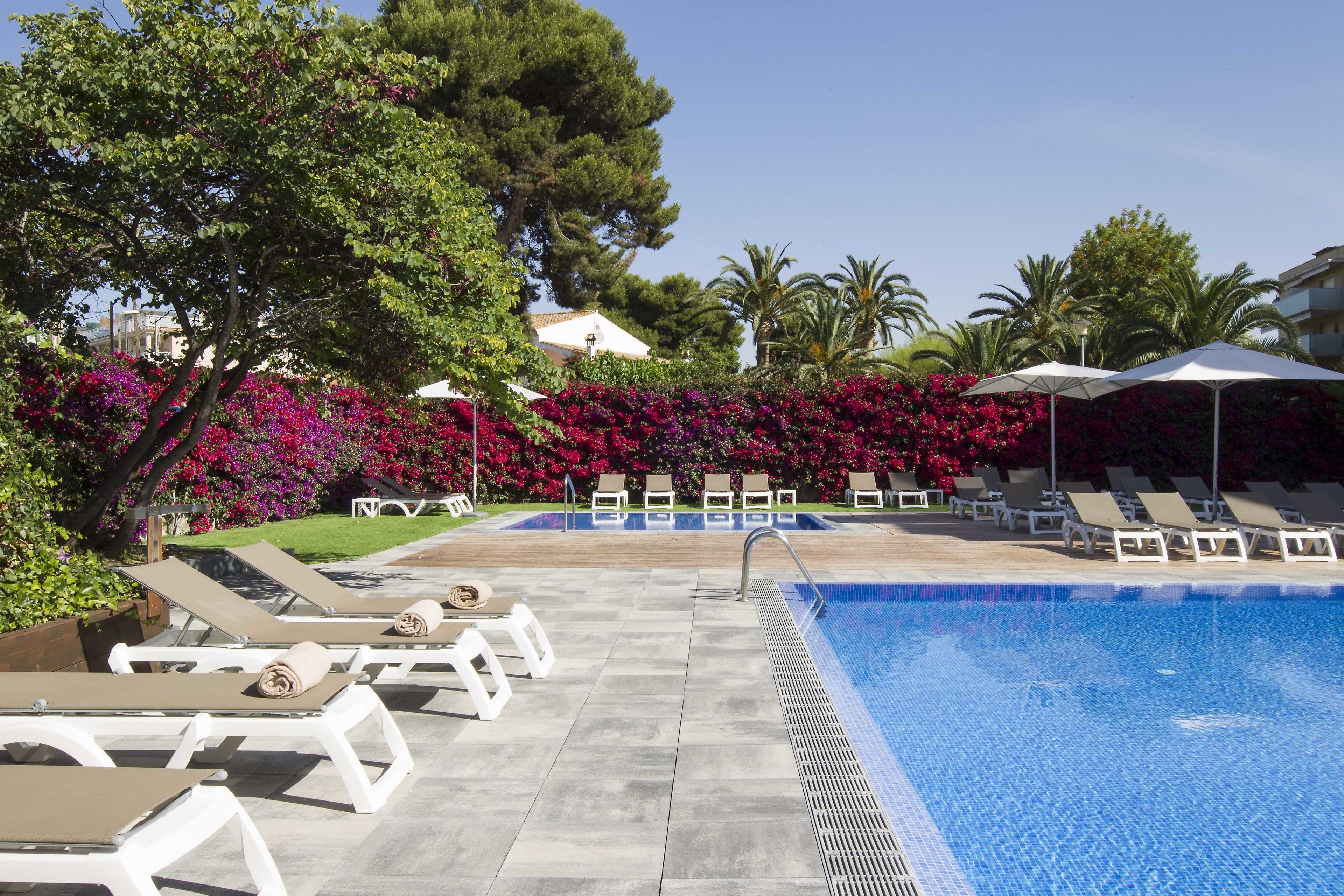 A pool area with lounge chairs and umbrellas, surrounded by lush greenery and flowering plants.