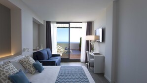 Habitació d'hotel amb llit, escriptori, cadira, televisió i un balcó amb vista al mar.