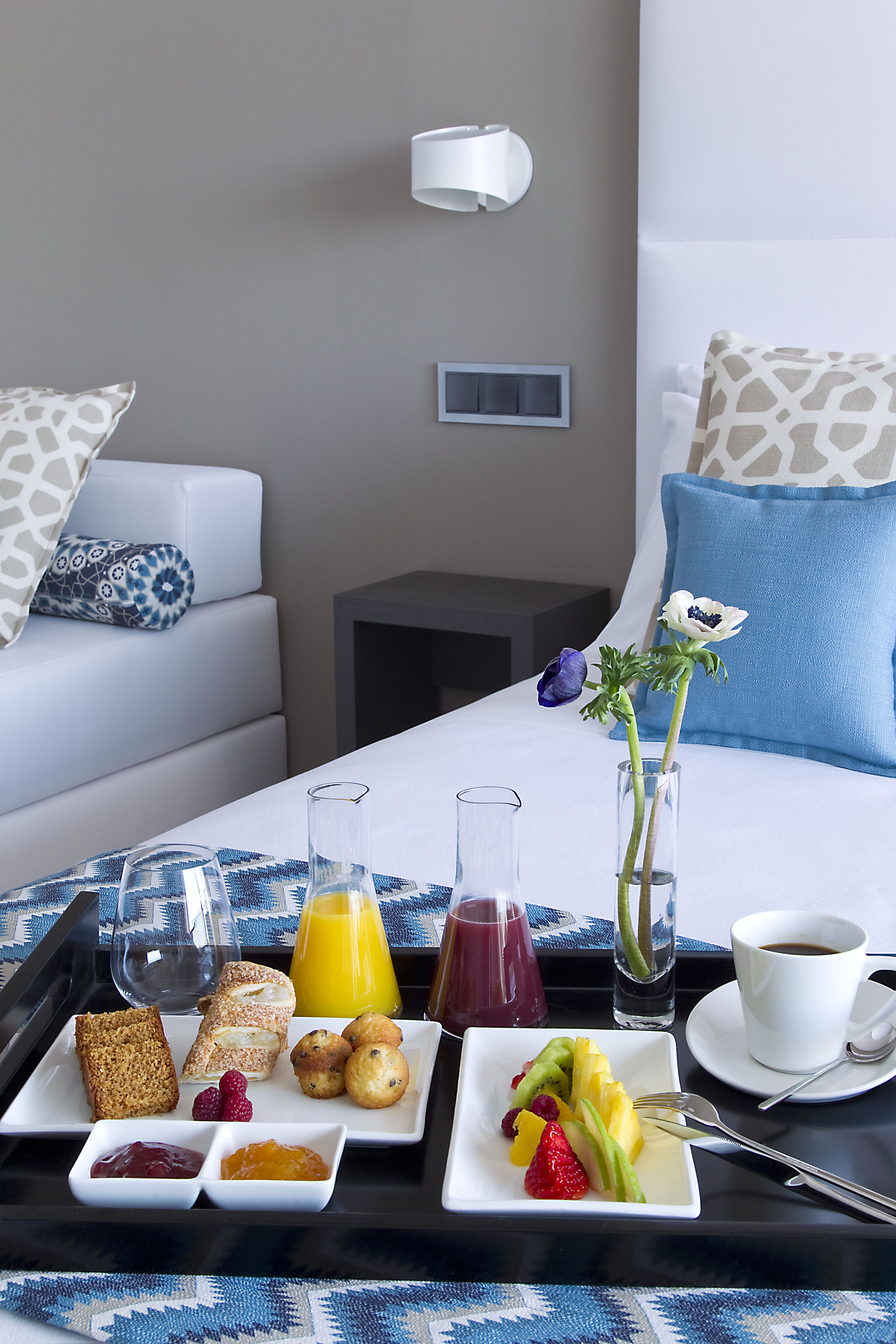 Una bandeja de desayuno ordenada con diversos alimentos y bebidas sobre una cama de hotel.