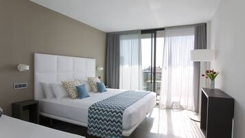 Een moderne hotelkamer met een groot bed, een nachtkastje, een bureau en uitzicht op de stad door grote ramen.