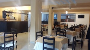 A restaurant interior with tables and chairs, a bar area, and a kitchen in the background. - Hotel Conquistador (Andahuaylas)