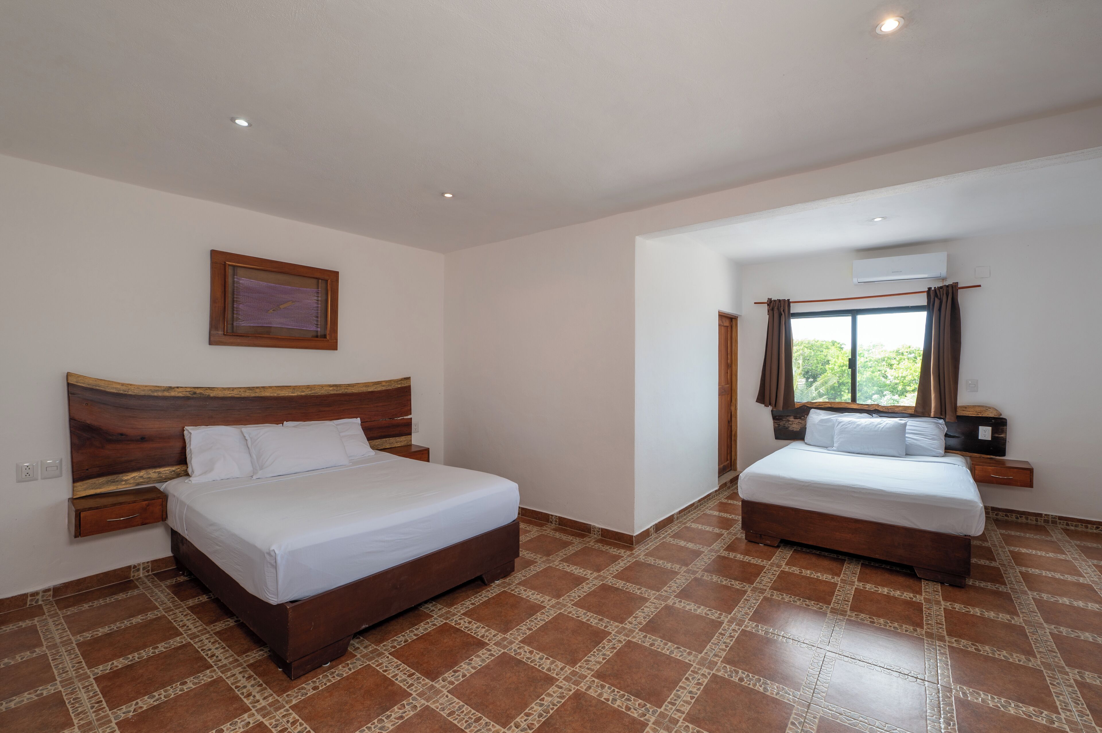 Habitació d'hotel amb dos llits, un capçal de llit de fusta, una tauleta de nit, un quadre encapçalat a la paret i una finestra amb cortines.