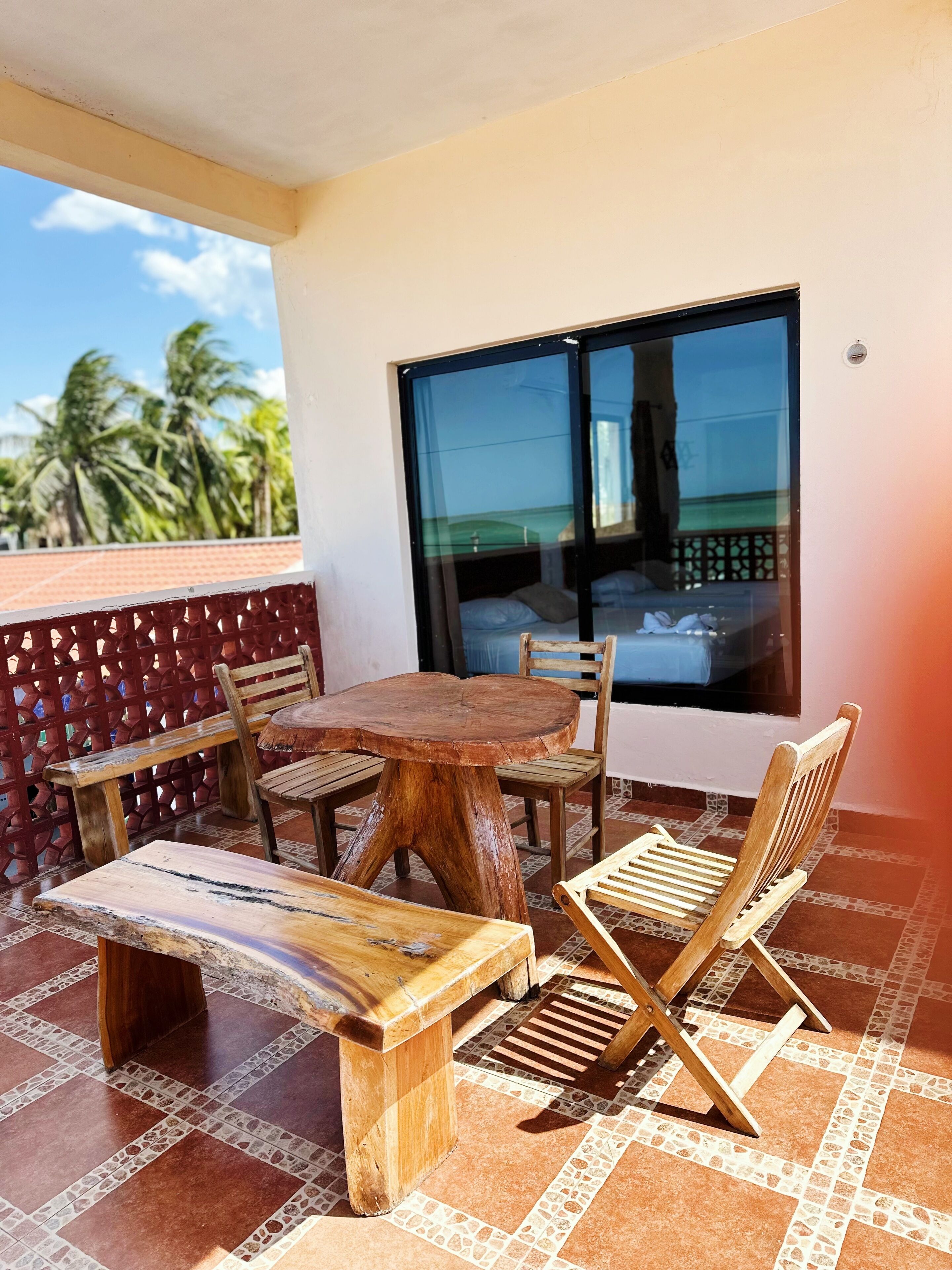 A wooden table and chairs on a tiled balcony with a view of palm trees.