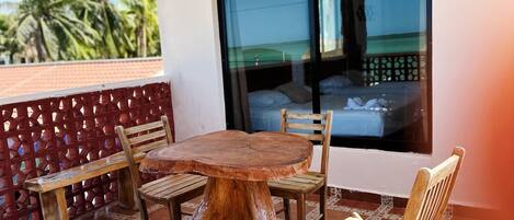 A wooden table and chairs on a tiled balcony with a view of palm trees.