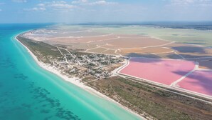 Vista aérea de una zona costera con playa, un pueblo y salinas rosadas.