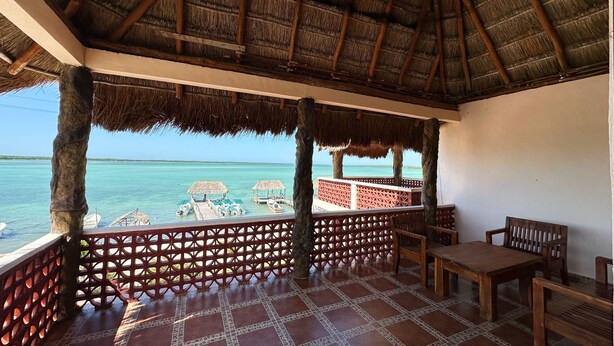Un espacio al aire libre cubierto, con suelo de baldosas, muebles de madera y vista al océano.