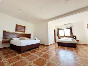 A hotel room with two beds, a large painting on the wall, and a window with curtains. - El Perico Marinero (Río Lagartos)