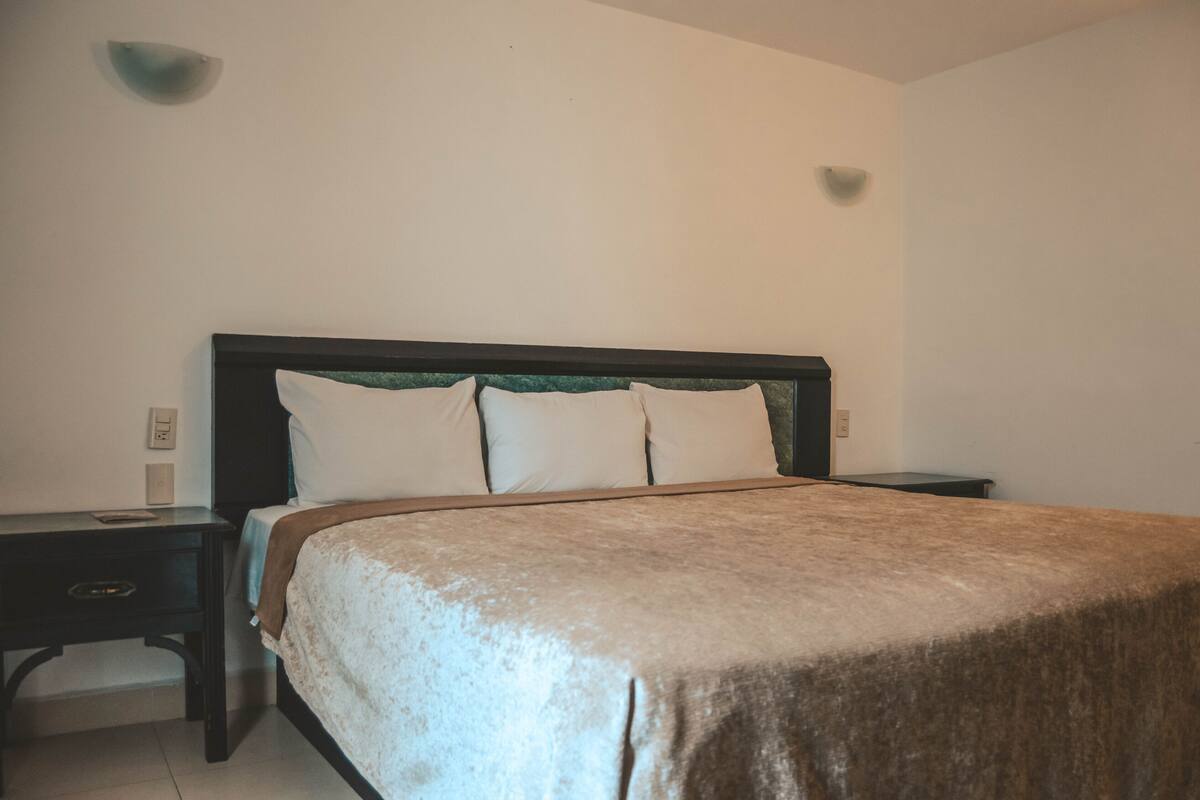 A neatly made bed with a dark headboard and white pillows in a simple room with white walls and minimal decor.