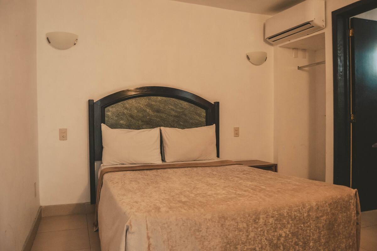 A single bed with a headboard, a bedside table, and an air conditioning unit mounted on the wall.