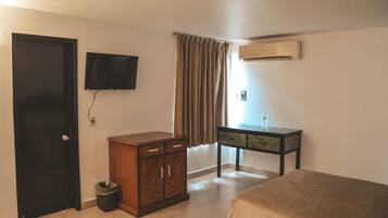 Habitación de hotel con una cama, un armario de madera, un televisor montado en la pared, una ventana con cortinas y un equipo de aire acondicionado.