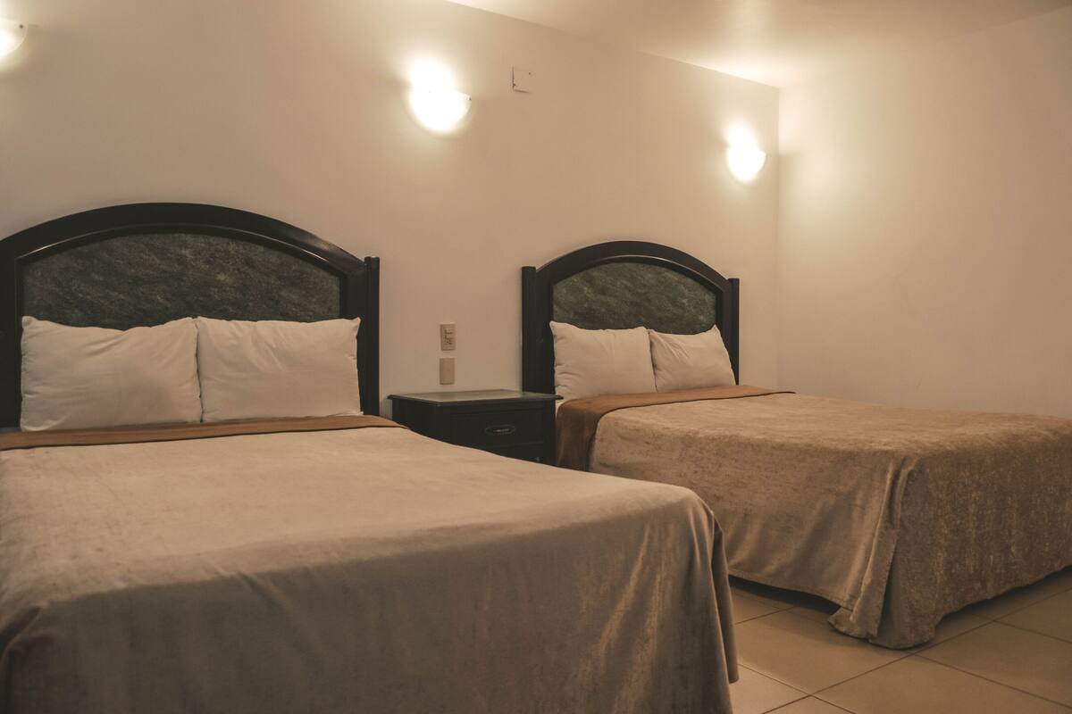 A hotel room with two single beds, a nightstand, and wall-mounted lights.