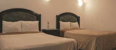 Habitación de hotel con dos camas individuales, una mesita de noche e iluminación en la pared.