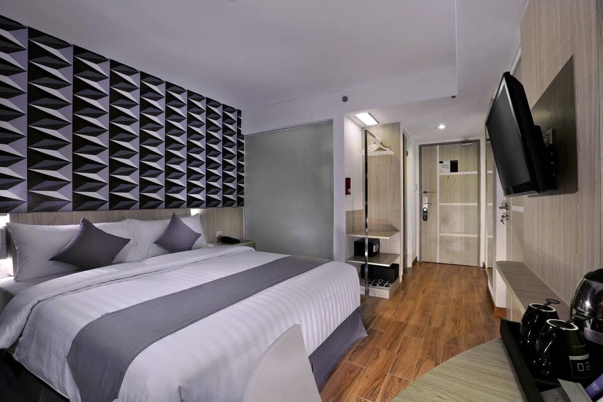 A modern hotel room with a large bed, a TV mounted on the wall, and a wooden floor.