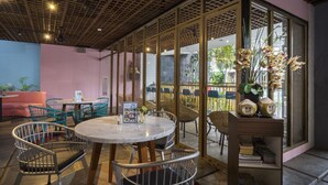 Ein Restaurant mit runden Tischen und Stühlen, einer Holzbalkendecke und großen Fenstern mit Blick ins Freie.