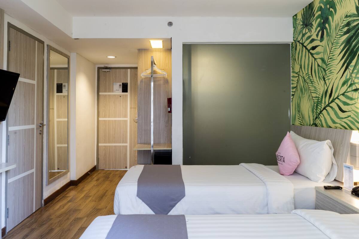 A hotel room with two beds, a wardrobe, a television, and a large plant.