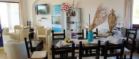 A hotel lobby with a dining area, a TV mounted on the wall, and a reception desk.