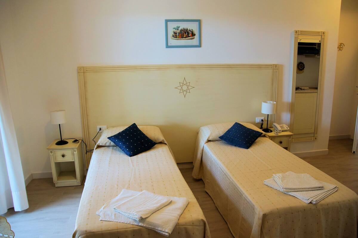 A hotel room with two single beds, a small bedside table with a lamp, a mirror, and a framed picture on the wall.