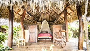 A thatched-roof structure with a bed and a swing chair. - Present Moment Retreat (Troncones)