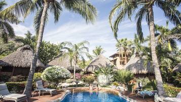 A pool area with lounge chairs, palm trees, and thatched-roof structures.
