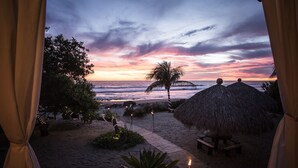 A beach view with a palm tree, thatched umbrellas, and a sunset. - Present Moment Retreat (Troncones)