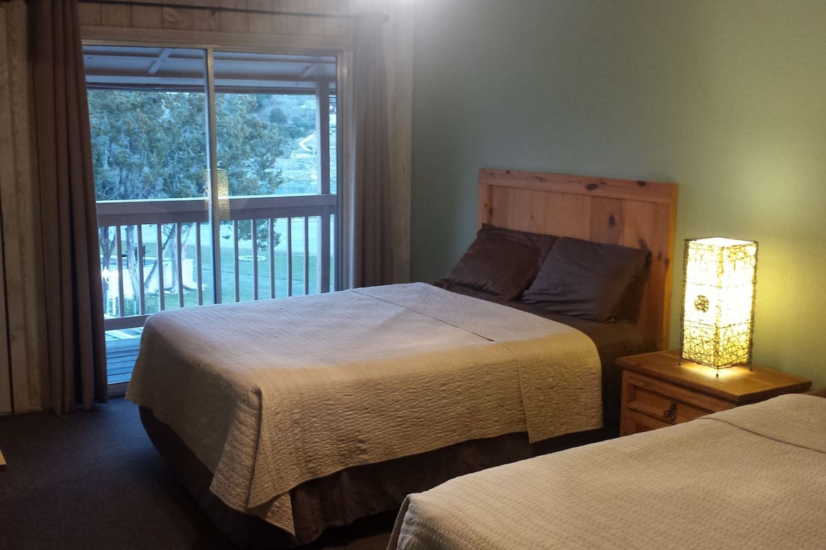 A bedroom with a bed, a nightstand, a lamp, a window, and a door.
