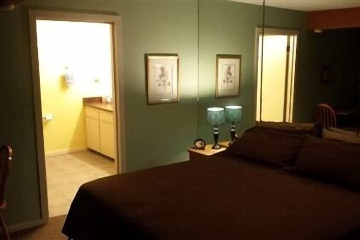 A bedroom with a large bed, a nightstand with two lamps, and two framed pictures on the wall.