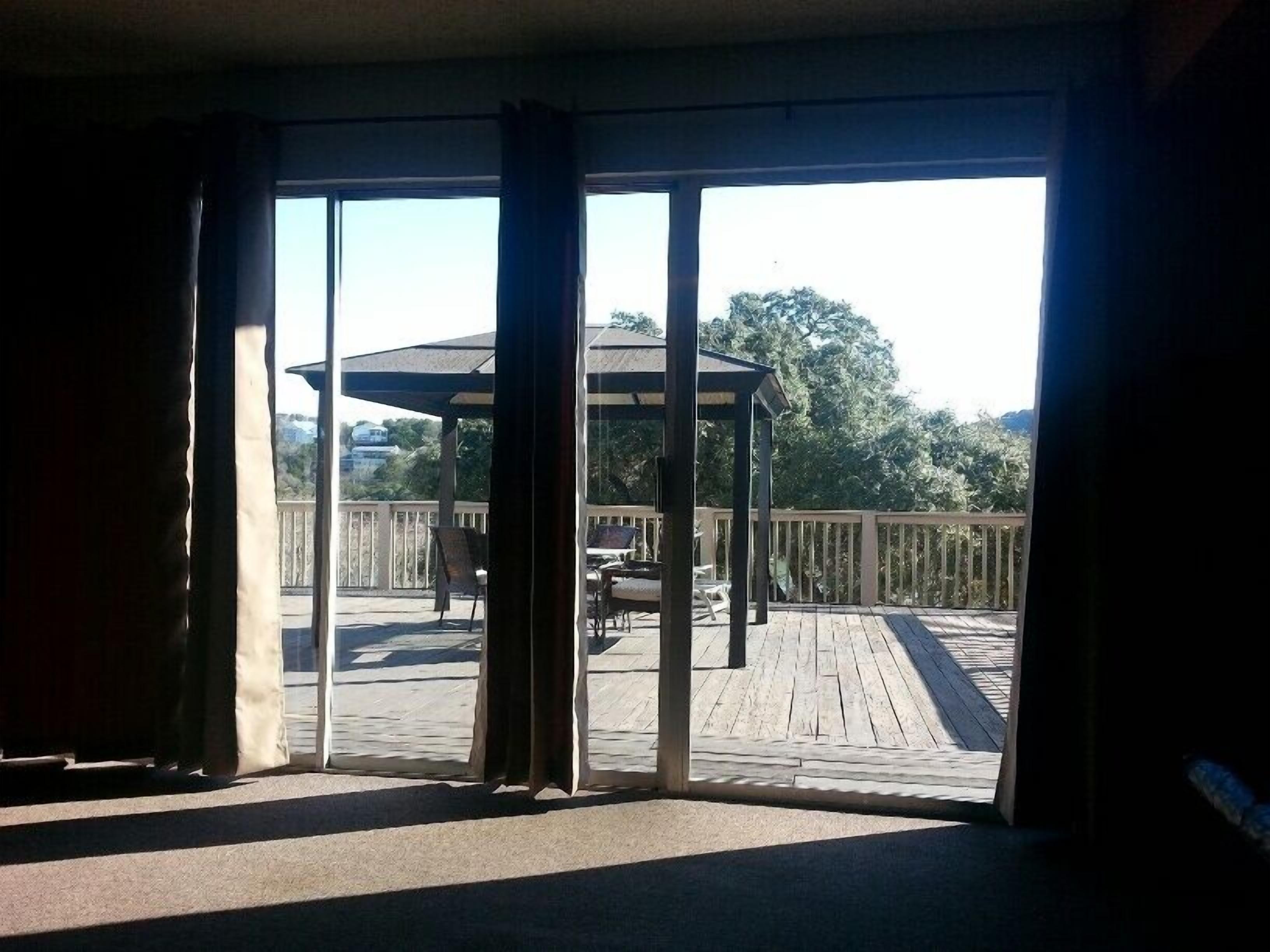 Vista desde una habitación con grandes puertas de vidrio a un área exterior con terraza, un pabellón, sillas y una mesa.