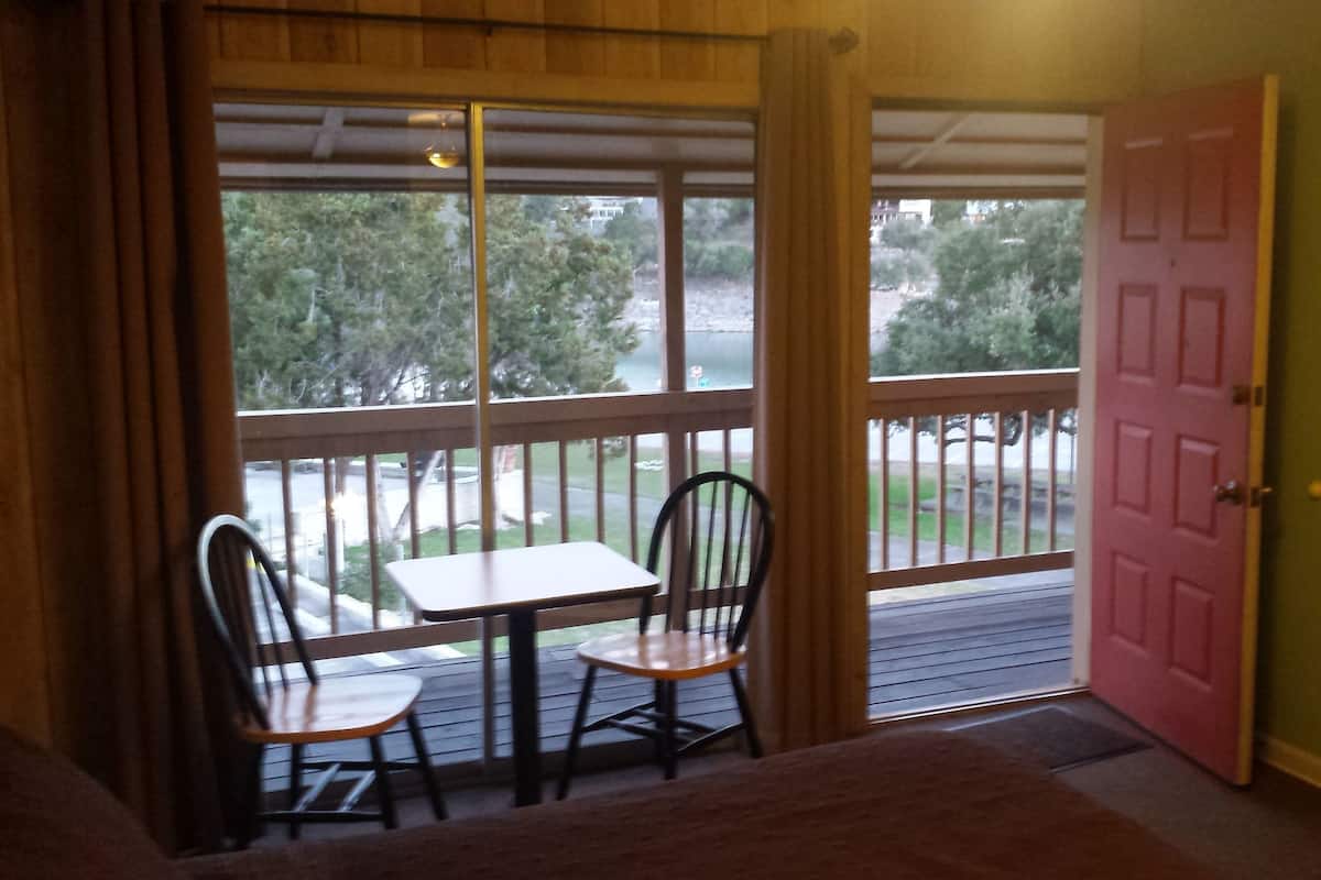 A room with a sliding glass door leading to a balcony, a small table with two chairs, and a wooden dresser with a television.
