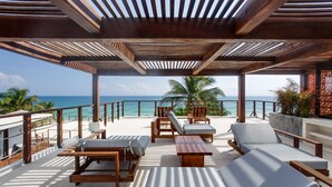 A covered outdoor seating area with wooden furniture and a view of the ocean. - Lula Tulum, a Small Luxury Hotel (Tulum)