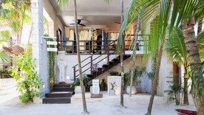 L’entrée d’un hôtel, avec un escalier, des palmiers et une enseigne accueillant les clients.
