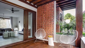 A modern living room with a wooden ceiling, a glass door leading outside, and two white wire chairs with a fruit bowl on a small table. - Lula Tulum, a Small Luxury Hotel (Tulum)