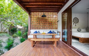 A wooden deck with a bench and table, a wooden ceiling, and a room with a bed and a wall-mounted dreamcatcher. - Lula Tulum, a Small Luxury Hotel (Tulum)